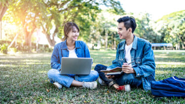 芝生の上でパソコンを開いて談笑する男女の写真